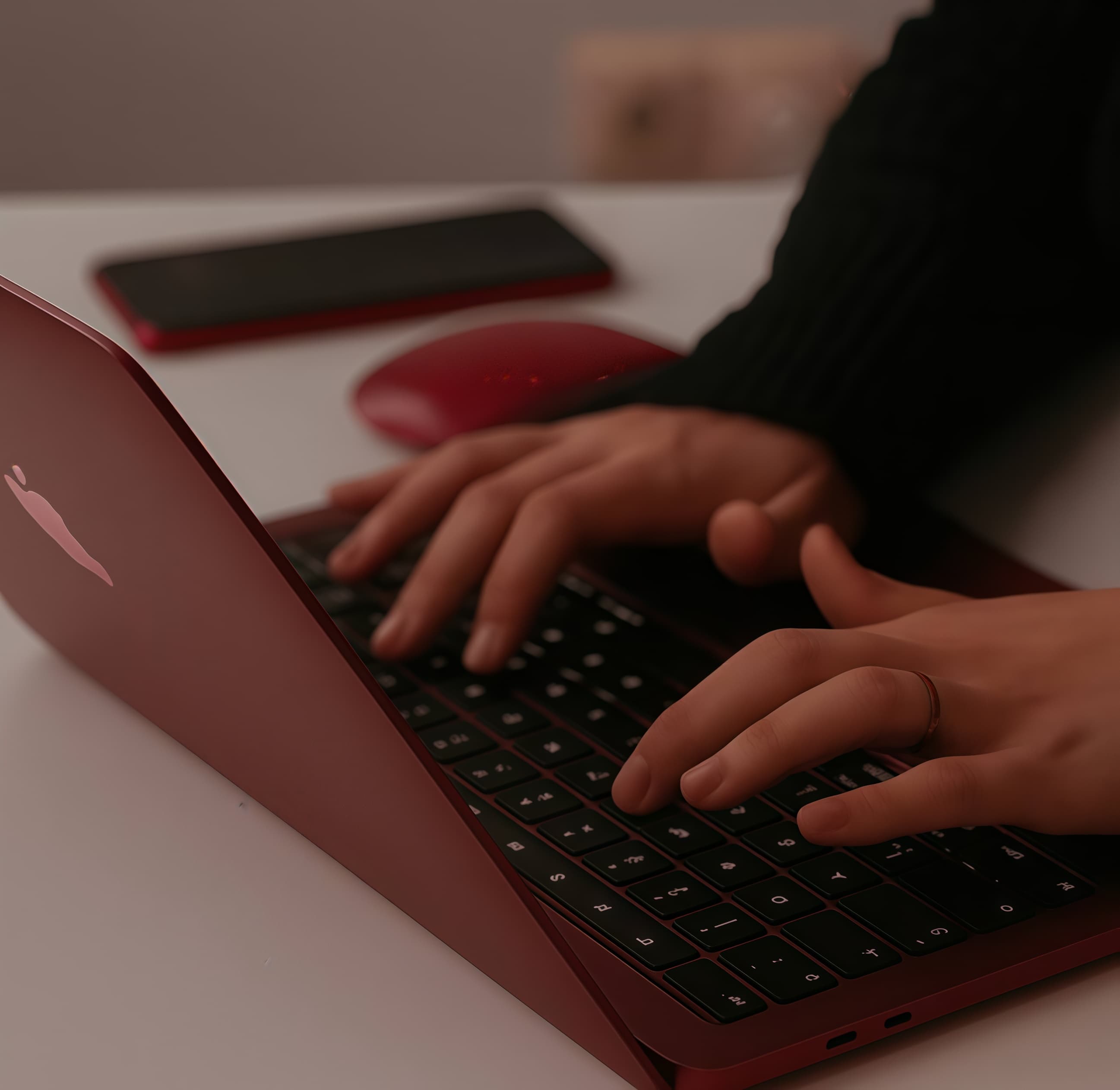 Hands typing on a slim red laptop keyboard next to a red computer mouse.